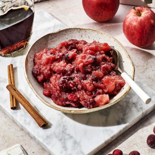 Cooked apple cranberry sauce in a serving bowl with a spoon.