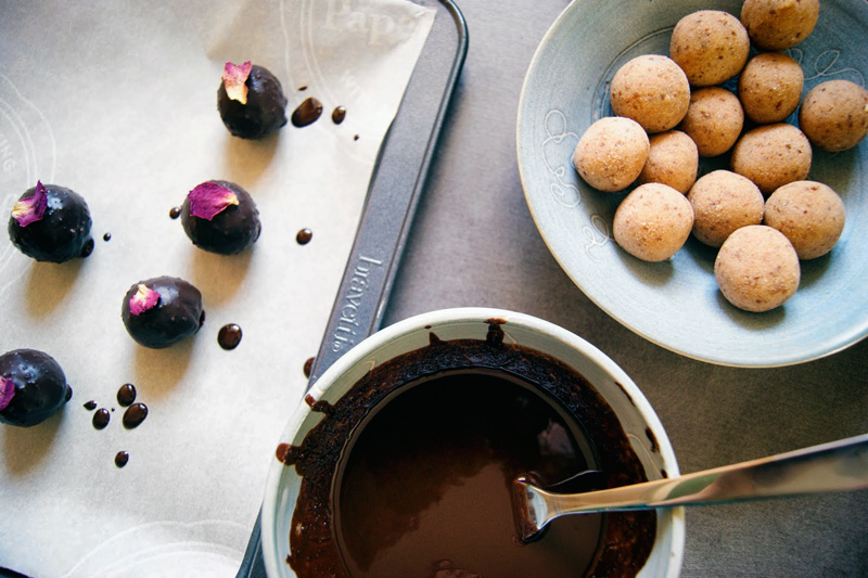 Marzipan balls in one bowl, melted chocolate in another, coated balls on a tray.