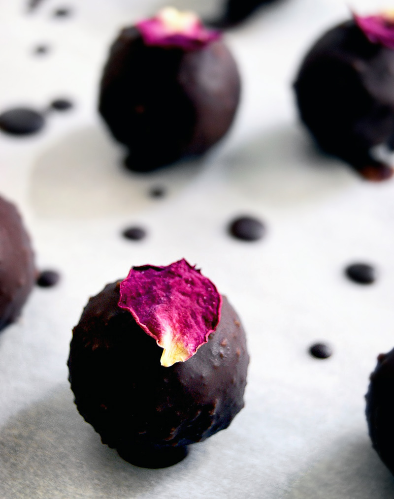 A marzipan truffle coated in chocolate topped with a rose petal.