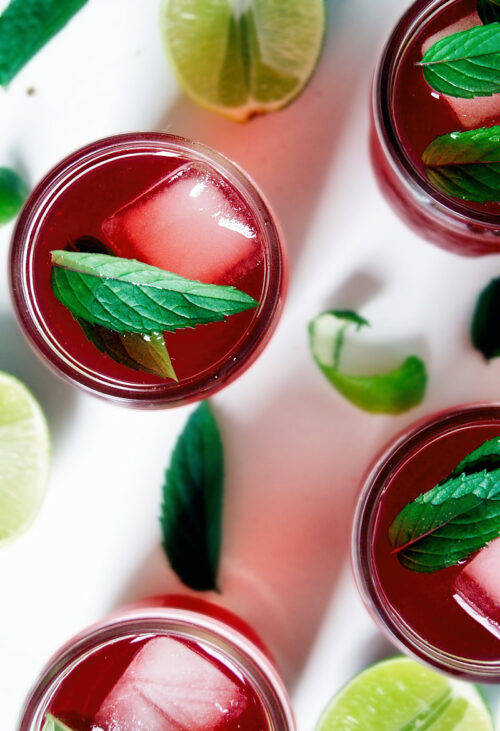 Several glasses of pink tea with ice and mint leaves.