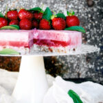 Raw strawberry layer cake on a cake stand, topped with fresh berries.