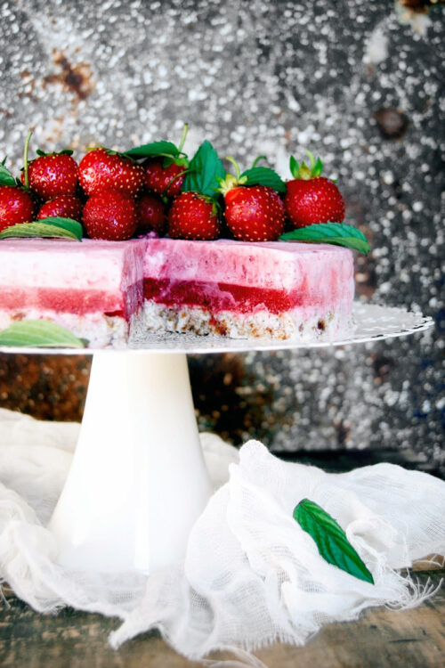 Raw strawberry layer cake on a cake stand, topped with fresh berries.