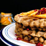 Close up of a stack of waffles topped with orange and pomegranate.
