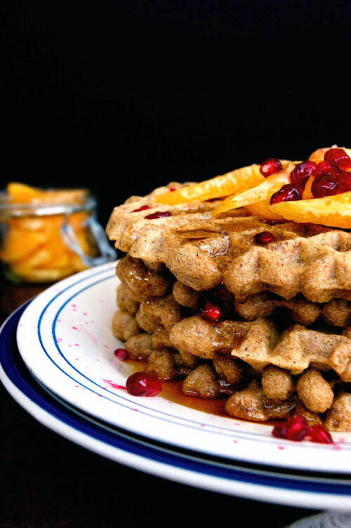 Close up of a stack of waffles topped with orange and pomegranate.