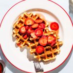 Two waffles on a plate with sliced strawberries.