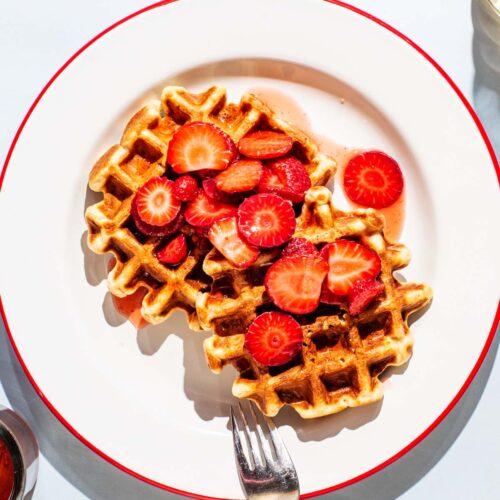 Two waffles on a plate with sliced strawberries.