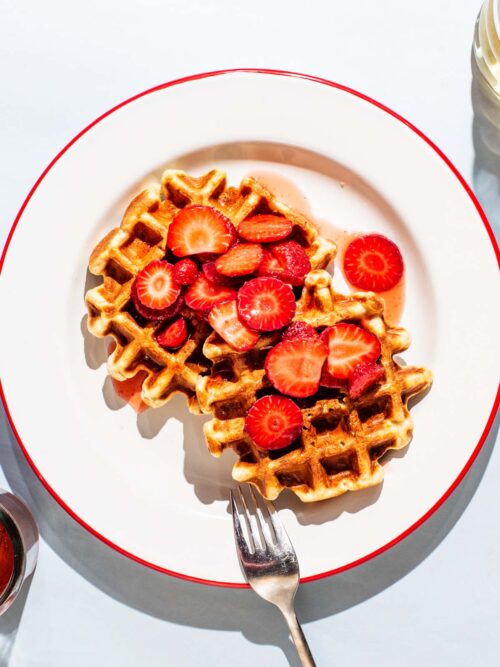 Two waffles on a plate with sliced strawberries.