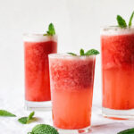 Pink strawberry slush in three glasses, topped with mint leaves on a white background.