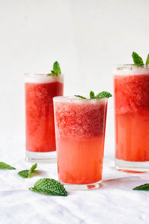 Pink strawberry slush in three glasses, topped with mint leaves on a white background.
