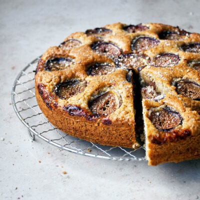 Fig-topped cake on a wire rack with one slice cut.