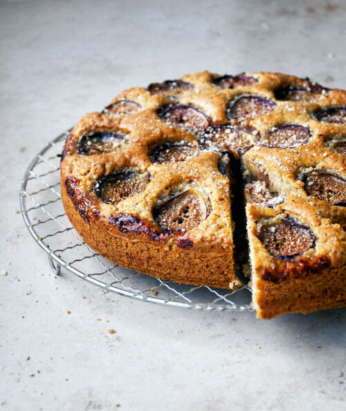 Fig-topped cake on a wire rack with one slice cut.