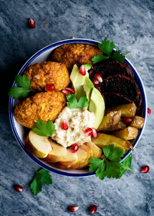 Top down view of a bowl with falafel, potatoes, and other vegetables.