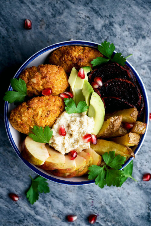 Top down view of a bowl with falafel, potatoes, and other vegetables.