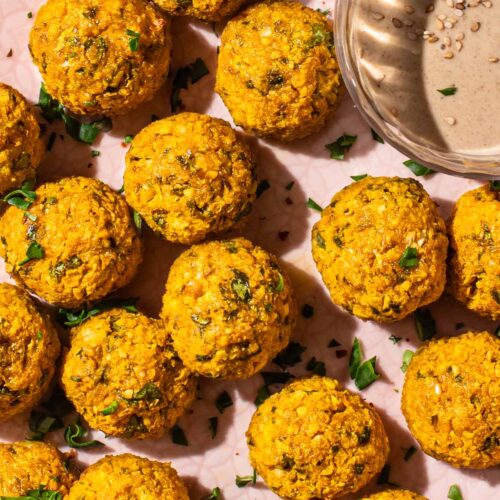 Close up of several orange falafel on a pink tray.