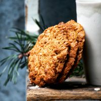 Three big honey oat cookies leaning against a white tumbler.