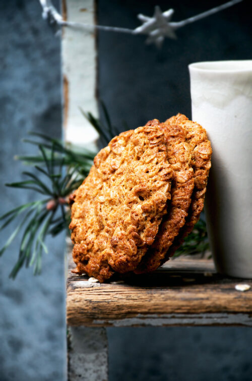 Three big honey oat cookies leaning against a white tumbler.