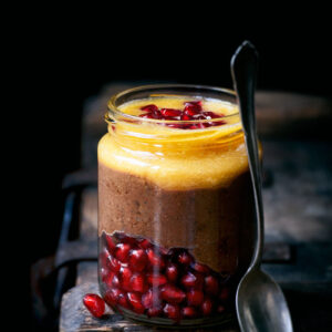 A jar of chocolate pudding layered with orange juice and pomegranate seeds.