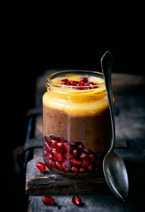 A jar of chocolate pudding layered with orange juice and pomegranate seeds.