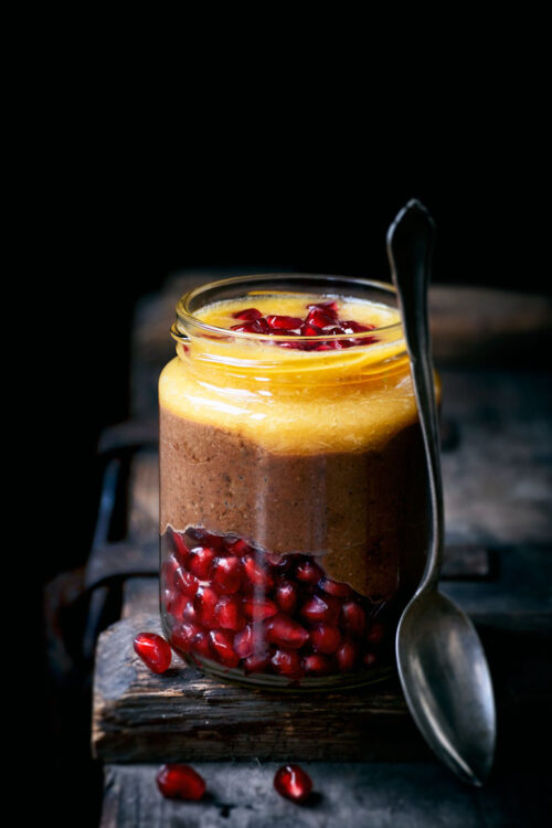A jar of chocolate pudding layered with orange juice and pomegranate seeds.