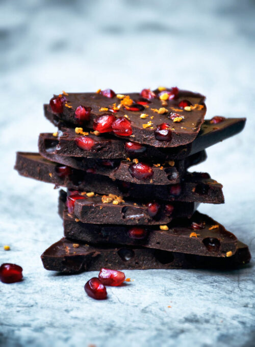 A stack of pieces of chocolate with pomegranate seeds and orange zest.