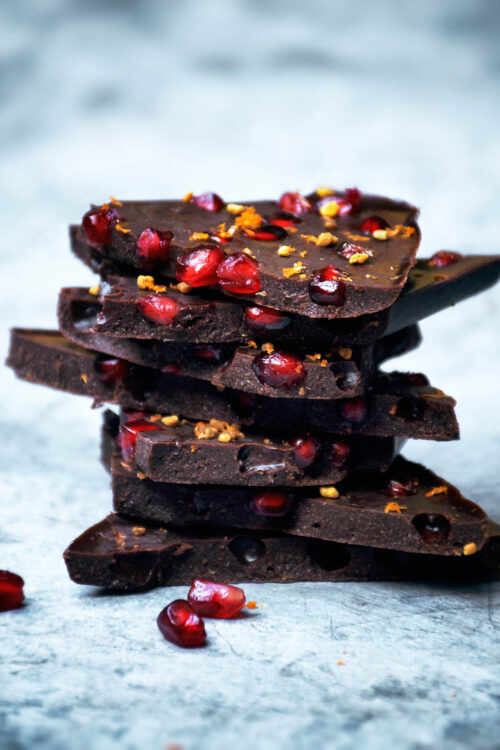 A stack of pieces of chocolate with pomegranate seeds and orange zest.