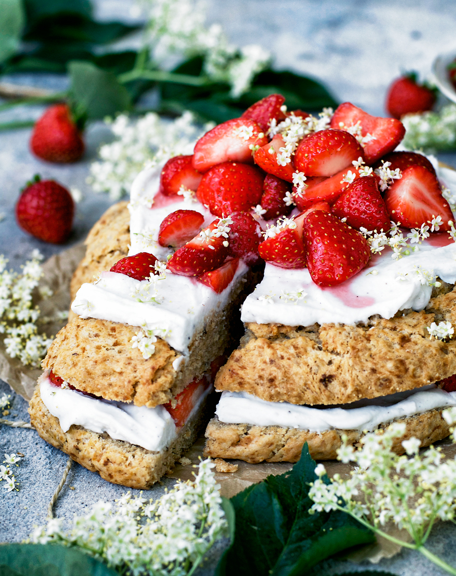 Giant vegan scone cake, front view, layered with coconut whipped cream, strawberries, and elderflower, one slice cut