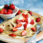 Crepes on a plate topped with cream and strawberries.