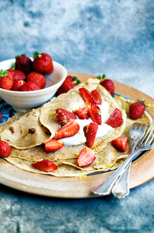 Crepes on a plate topped with cream and strawberries.