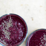 Two glasses filled with a dark purple blueberry smoothie, topped with chia seeds, top down view.
