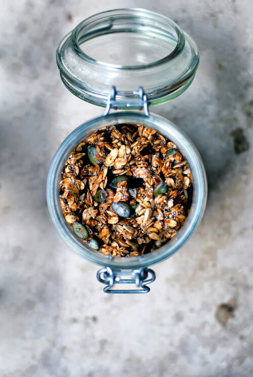 Olive oil granola with pumpkin seeds in a glass jar, top down view, on stone surface.