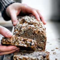 Woman's hands taking a slice of banana bread from the loaf.