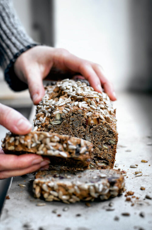 Woman's hands taking a slice of banana bread from the loaf.