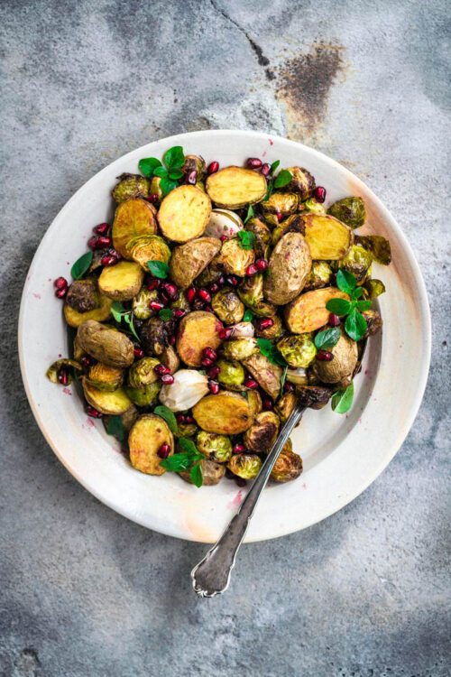A plate of roasted potatoes and brussels sprouts with herbs.
