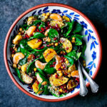 Spinach salad in a serving bowl with yellow beets, pomegranate, and mandarin pieces.