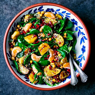 Spinach salad in a serving bowl with yellow beets, pomegranate, and mandarin pieces.
