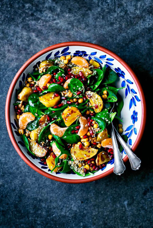 Spinach salad in a serving bowl with yellow beets, pomegranate, and mandarin pieces.