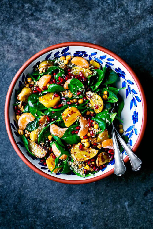 Spinach salad in a serving bowl with yellow beets, pomegranate, and mandarin pieces.