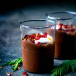 Two glasses of chocolate mousse topped with yogurt and pomegranate.