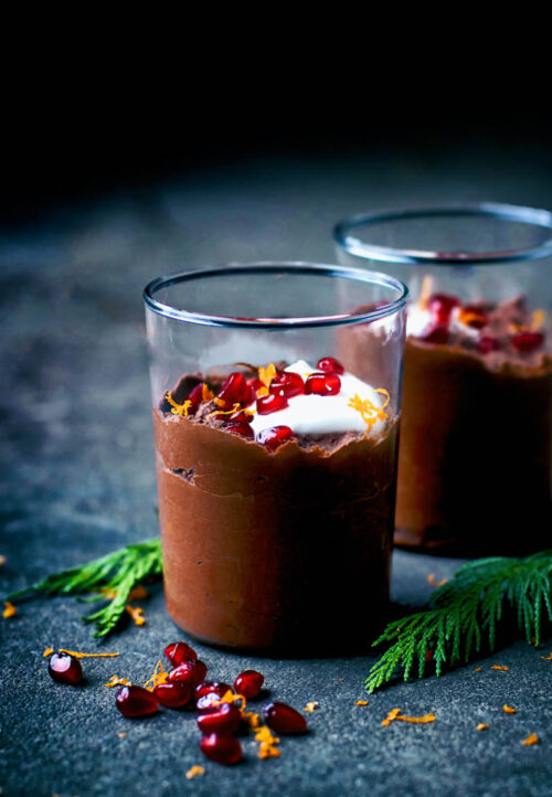 Two glasses of chocolate mousse topped with yogurt and pomegranate.