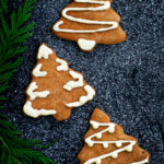 Three Christmas tree cookies with white chocolate decoration.