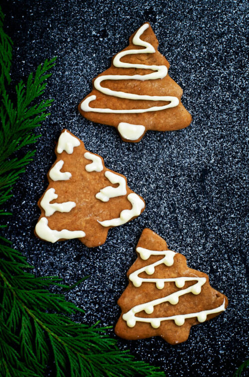 Three Christmas tree cookies with white chocolate decoration.