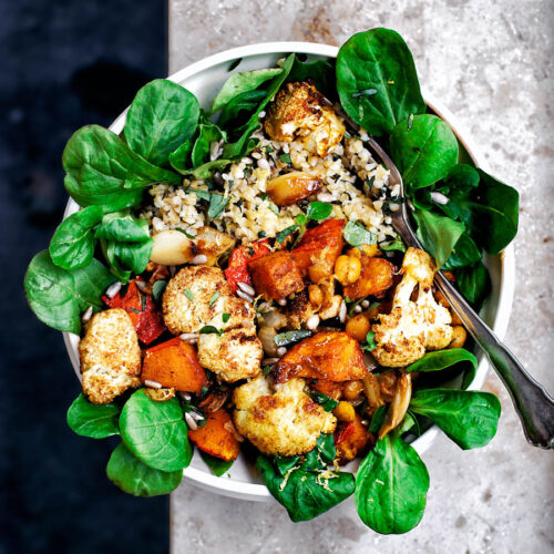 A bowl filled with salad, roasted vegetables, and bulgur.