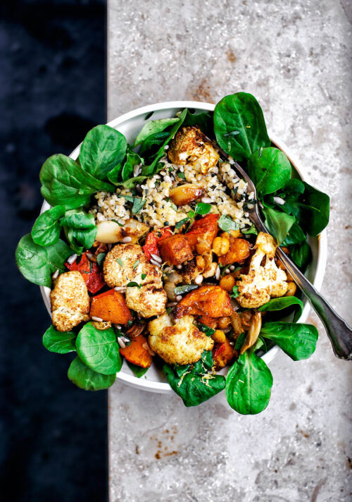 A bowl filled with salad, roasted vegetables, and bulgur.