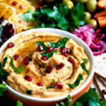 Mezze board with sweet potato hummus, regular hummus, crackers, vegetables, and fruit.