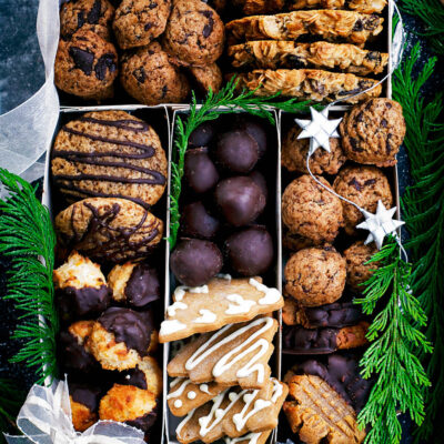 Several types of cookies arranged in a box with holiday decorations.