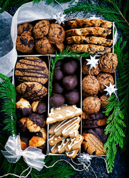 Several types of cookies arranged in a box with holiday decorations.