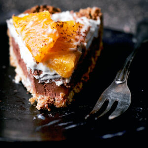A slice of a chocolate tart on a small plate topped with cream and orange slices.