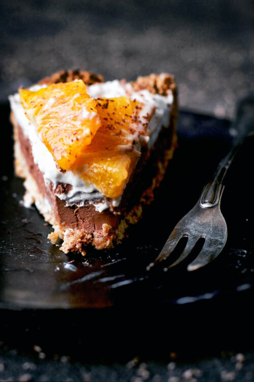A slice of a chocolate tart on a small plate topped with cream and orange slices.