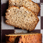 A loaf of coconut bread on a tile surface, top down view, with two slices cut.