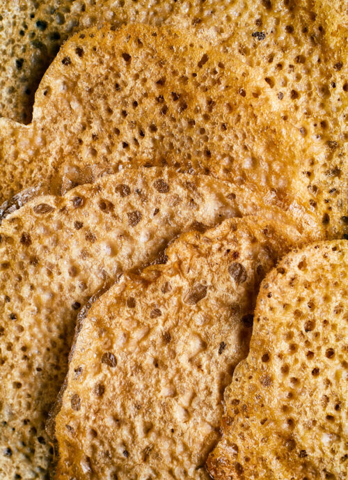 Close up of several thin, bubbly pancakes arranged in a fan.